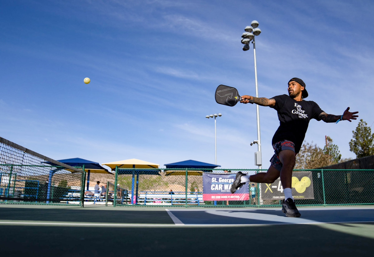 Black player hitting a pickleball on court